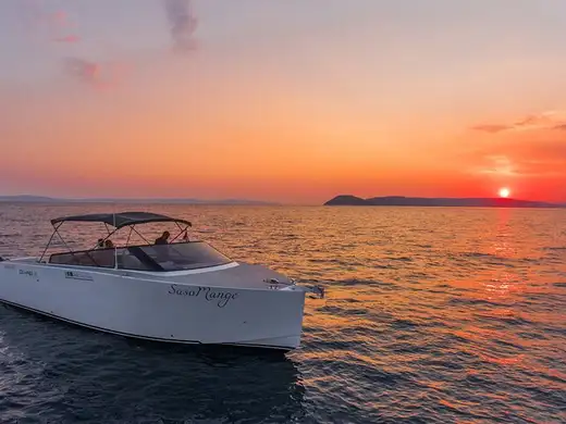 The boat lying still on flat water as the sun sets behind an island